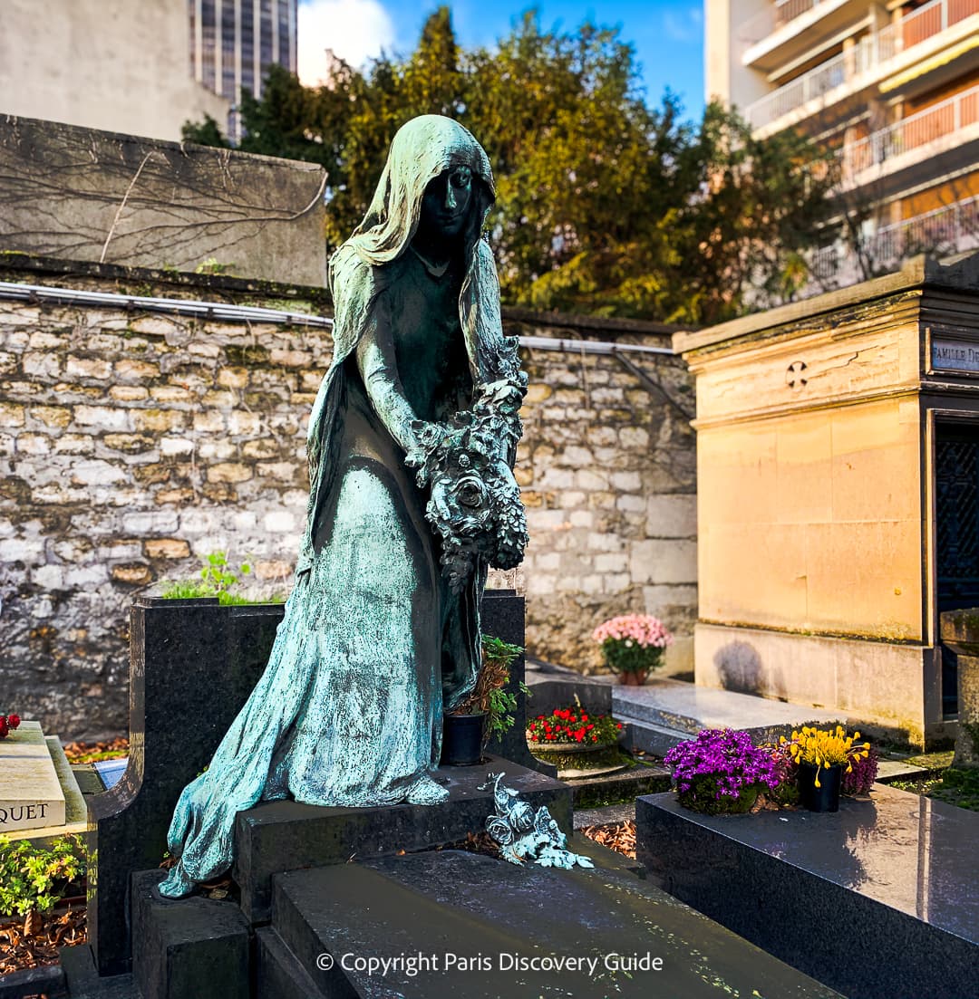 Toussaint flowers on graves and funerary sculpture of a woman laying flowers on a grave at Montparnasse Cemetery