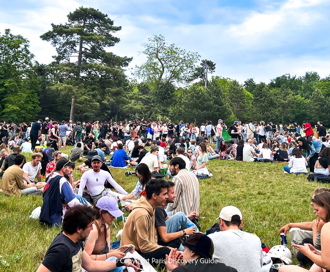 People sitting on grass in Bois de Vincennes waiting for a concert to begin